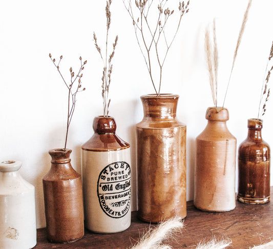 Collection of vintage-style ceramic bottles with dried plants on a wooden surface.